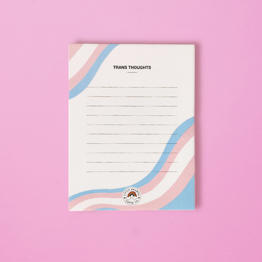 A LGTBQ notepad with the trans pride flag colors printed on the front. Text reads trans thoughts and has lines for writing. A cute trans pride notepad