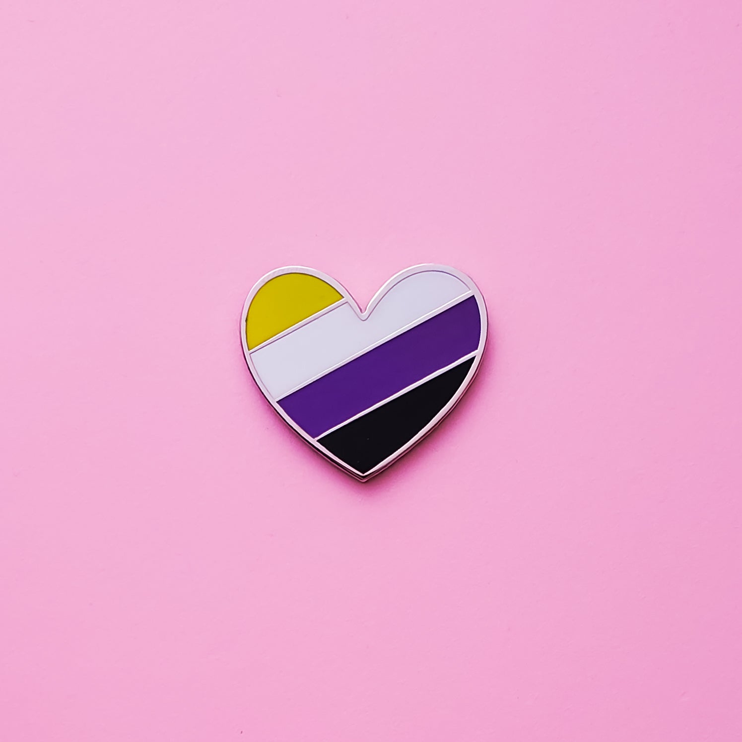 Heart-shaped Non-binary Pride Pin on a pink background. This Non-binary Pin or enby pin is has vibrant non binary pride colours set in a polished nickle metal. Non binary pride pin colours are yellow, purple, white and black. Non-binary Heart Pin - LGBTQ Pride Pins | Little Rainbow Paper Co