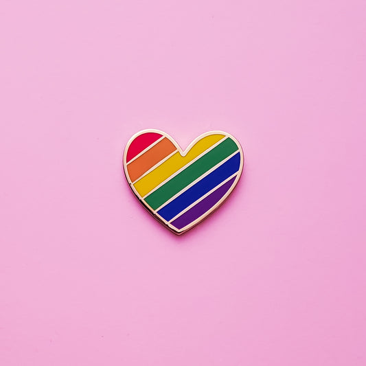 Heart-shaped Gay Pride Pin on a pink background. This LGBTQ pride pin is has vibrant rainbow pride colours set in a polished gold metal. Gay pride pin colours are red, orange,  yellow, green blue and purple.Rainbow Heart Pin - LGBTQ Pins For Sale | Little Rainbow Paper Co