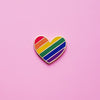 Heart-shaped Gay Pride Pin on a pink background. This LGBTQ pride pin is has vibrant rainbow pride colours set in a polished gold metal. Gay pride pin colours are red, orange,  yellow, green blue and purple.Rainbow Heart Pin - LGBTQ Pins For Sale | Little Rainbow Paper Co