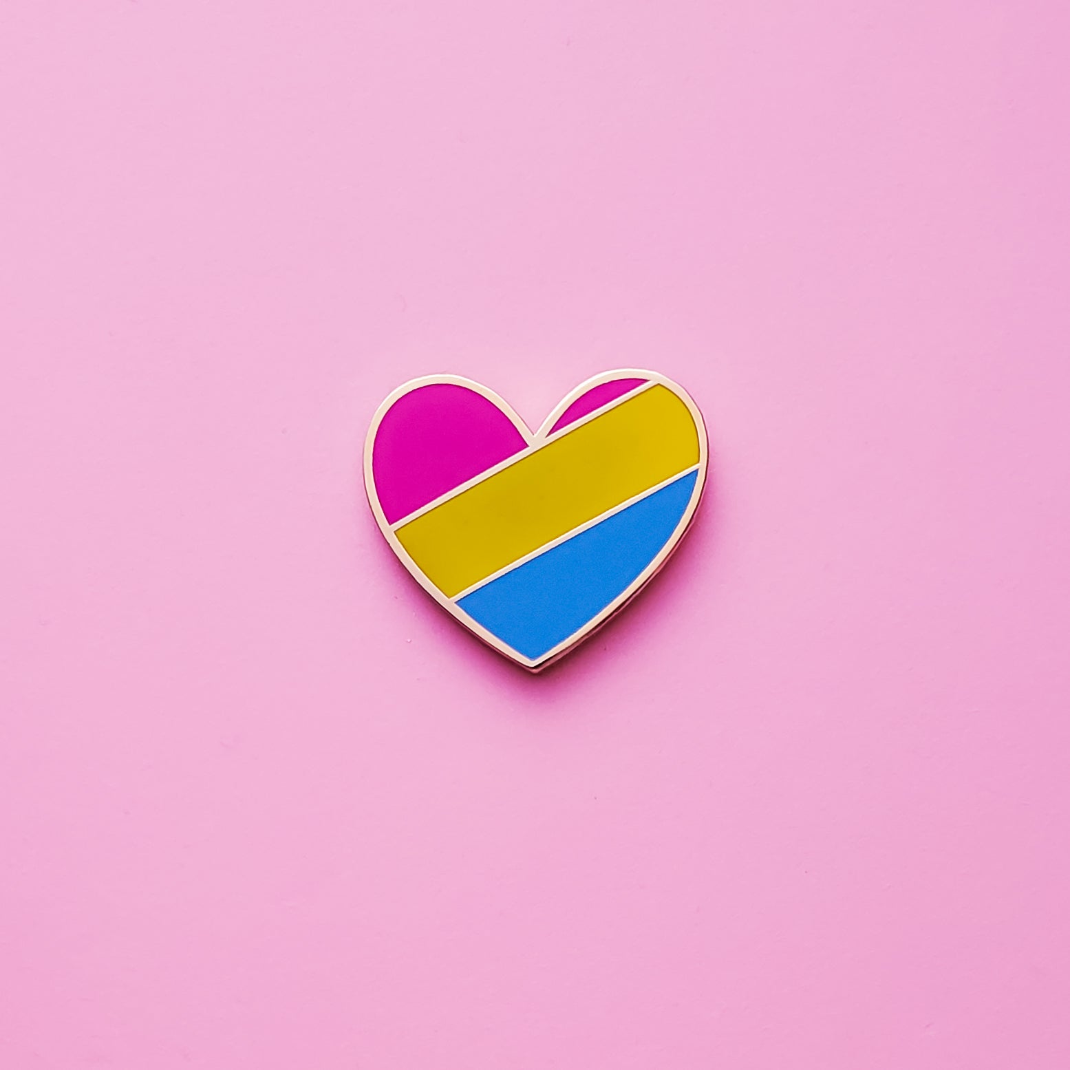 Heart-shaped Pansexual Pride Pin on a pink background. This Pansexual pin is has vibrant Pan pride colours set in a polished gold metal. Pan pride pin colours are pink, yellow and blue. Pan Heart Pin For Sale - LGBTQ Accessories  | Little Rainbow Paper Co