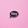 A Speech-bubble shaped They Pronoun Pin on a pink background. This They Pronoun Pin has black glitter enamel set in a polished gold metal. They Pronoun Pin For Sale - LGBTQ Accessories  | Little Rainbow Paper Co