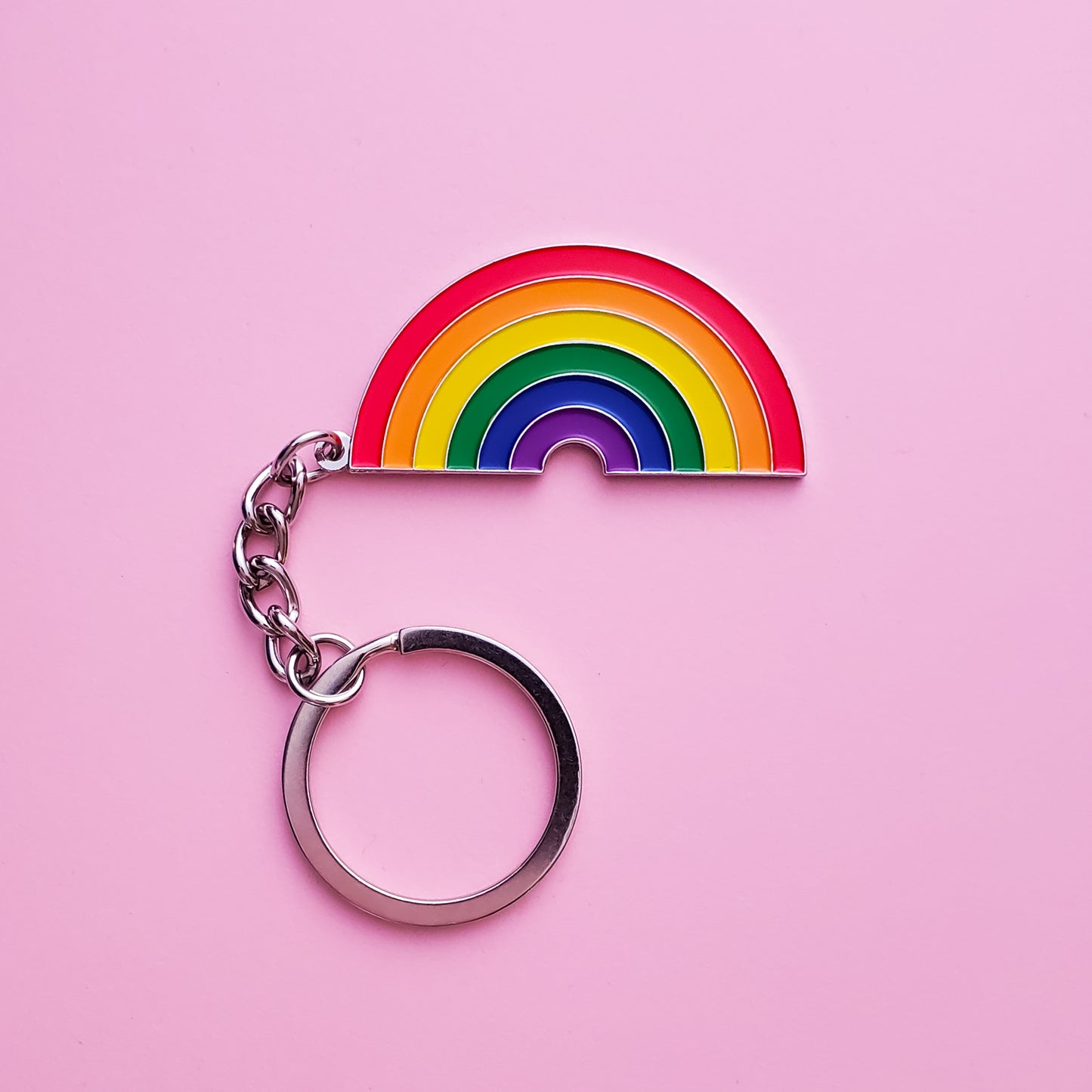 A rainbow keychain set on a pink background. This LGBTQ keychain is has vibrant rainbow pride colours set in a polished silver metal. Gay pride keychain colours are red, orange,  yellow, green blue and purple. Rainbow Keychain - LGBTQ Accessories | Little Rainbow Paper Co