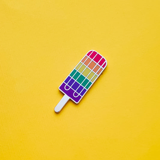 Popsicle-shaped Gay Pride Pin on a pink background. This LGBTQ pride pin is has vibrant rainbow pride colours set in a polished gold metal. Gay pride pin colours are red, orange,  yellow, green blue and purple. Rainbow Popsicle Pin - LGBTQ Pride Pins | Little Rainbow Paper Co