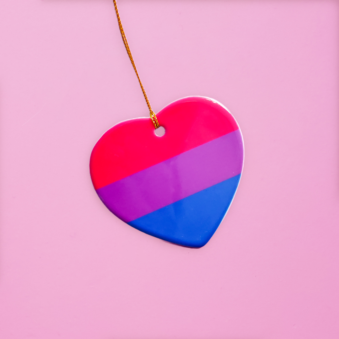 Ceramic heart shaped LGBTQ ornament with the bisexual pride colors on a pink background. Heart-shaped bi pride ornament