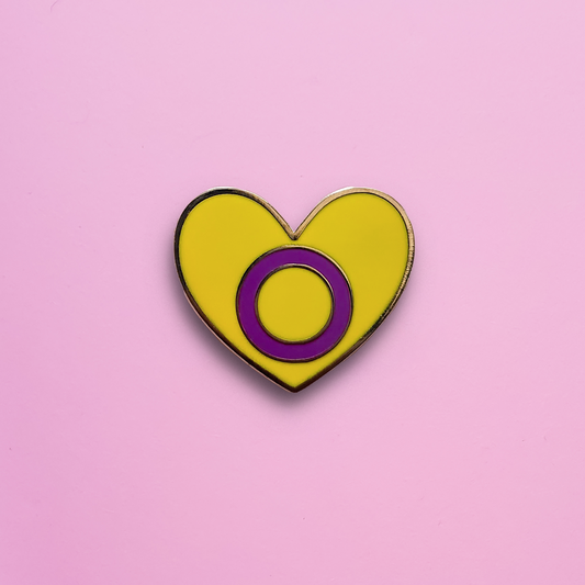 A Heart-shaped Intersex Pride Pin on a pink background. This Intersex pride pin is has vibrant Intersex pride colours set in a polished gold metal. Intersex pride pin colours are yellow with a  purple circle. Intersex Heart Pin - LGBTQ Pride Pins Canada | Little Rainbow Paper Co