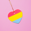 Ceramic heart shaped LGBTQ ornament with the pansexual pride colors on a pink background. Heart-shaped pan pride ornament