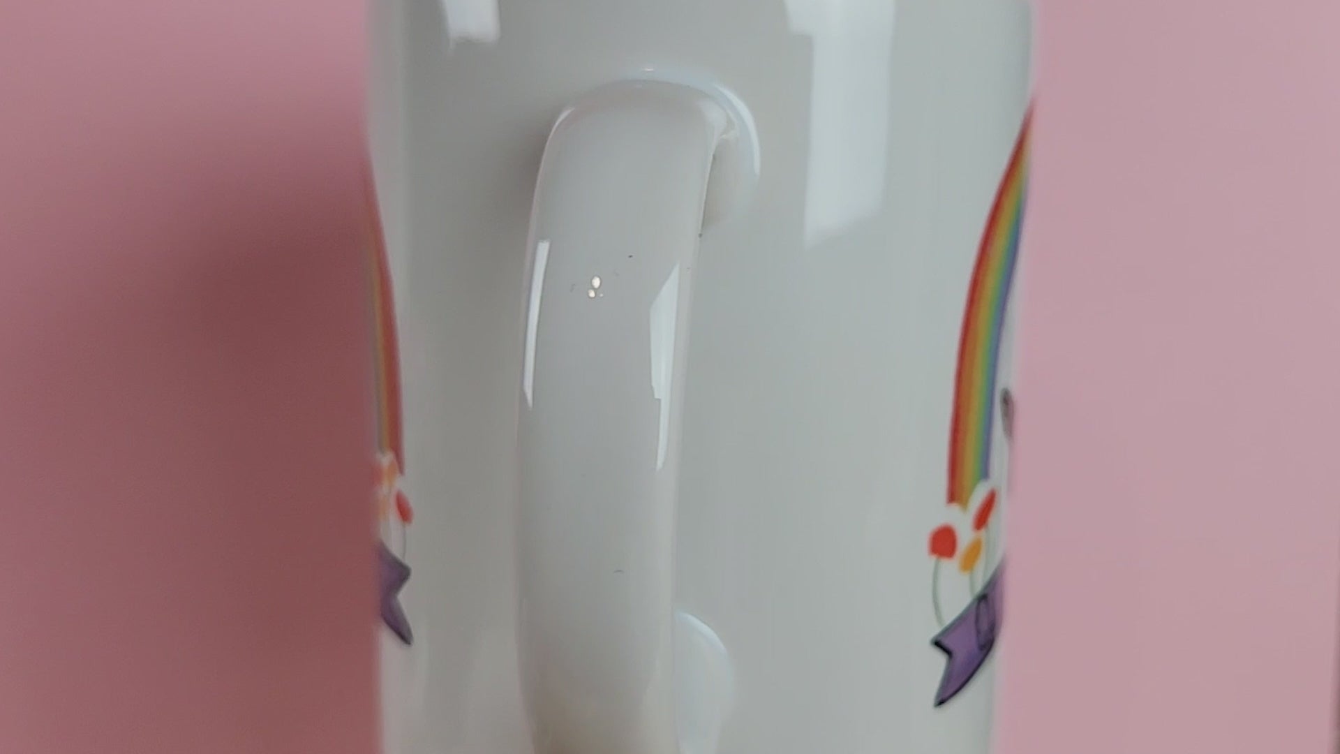 Video of a LGBTQ mug that has a deer sitting underneath a rainbow with a banner reading queer deer. Cute gay mug on a pink background