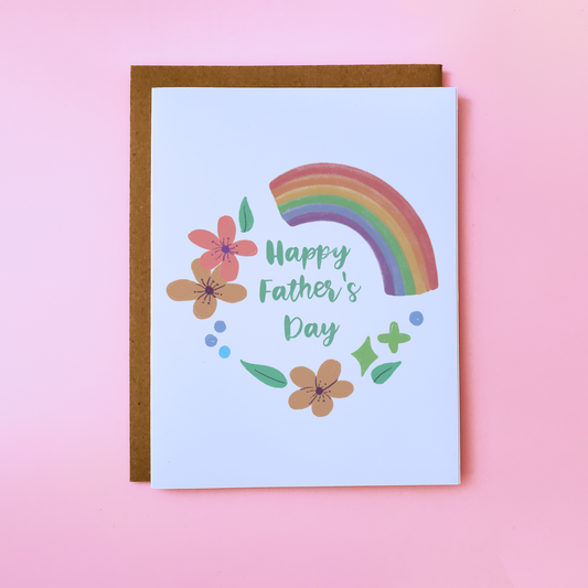 A LGBTQ Parent Card with a kraft envelope set on a pink background. This gay Father's Day Card features flowers and a rainbow and reads 'Happy Father's Day'.